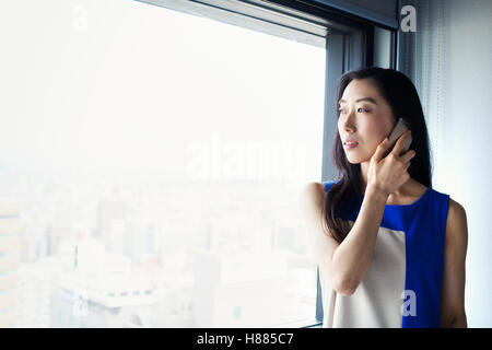 Eine Geschäftsfrau mit ihrem Smartphone und einem Fenster stand. Stockfoto