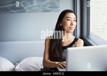 Eine Geschäftsfrau gekleidet, sitzt auf ihrem Bett mit einem Laptop. Stockfoto