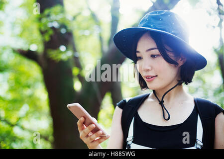 Junge Frau in einem Wald stehen, mit Hilfe eines Mobiltelefons. Stockfoto