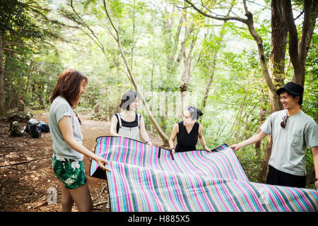 Drei junge Frauen und Menschen stehen in einem Wald, hält eine Picknickdecke. Stockfoto