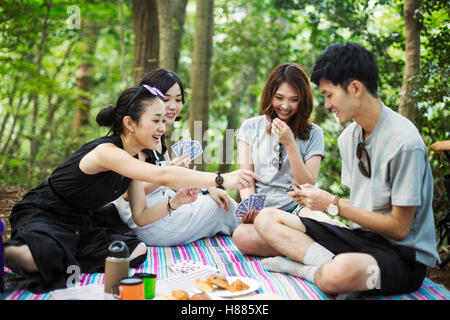 Drei junge Frauen und ein Mann sitzt in einem Wald, Spielkarten. Stockfoto