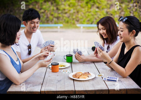 Drei junge Frauen und ein Mann sitzt an einem Tisch spielen Karten. Stockfoto