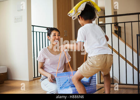 Haus der Familie. Eine Frau und ihr Sohn Sortieren der Wäsche, der junge Handtücher auf dem Kopf balancieren. Stockfoto