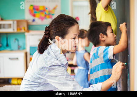 Eine Gruppe von Kindern, die mit ihrem Lehrer an die Tafel schreiben. Stockfoto