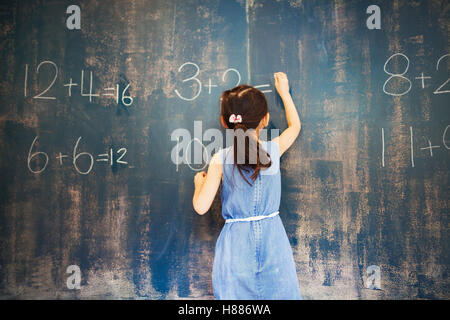 Eine Gruppe von Kindern in der Schule. Ein Mädchen mit Kreide auf eine Tafel schreiben. Stockfoto