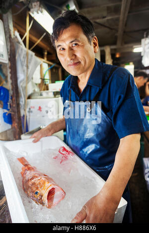 Eine traditionelle Fischmarkt in Tokio. ein Fischverkäufer hält eine Schachtel mit Eis mit einem frischen Fisch. Stockfoto