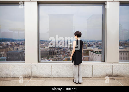 Eine Frau stand auf der Suche über eine Stadt von einem hohen Aussichtspunkt. Stockfoto