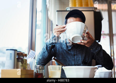 Ein Ramen-Nudel-Café in einer Stadt.  Ein Mann sitzt Essen Ramen-Nudeln aus einer großen Brühe Schüssel. Stockfoto