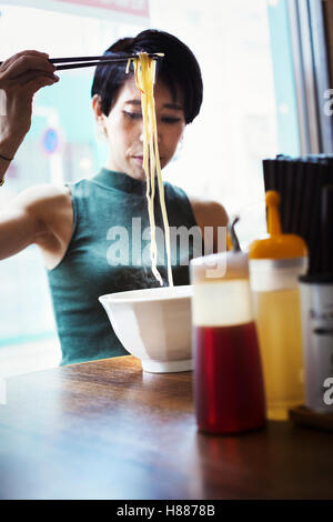 Ein Ramen-Nudel-Café in einer Stadt.  Eine Frau sitzt ein Ramen-Nudelgericht mit Stäbchen zu essen. Stockfoto