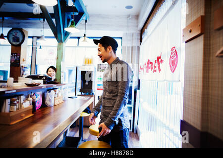 Ein Ramen-Nudel-Café in einer Stadt.  Kunden stehen an der Theke Essen bestellen. Stockfoto