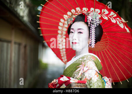 Eine Frau gekleidet im Stil traditionellen Geisha trägt einen Kimono und Obi, hält einen rotes Papier Sonnenschirm. Stockfoto