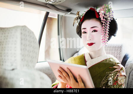 Eine Frau gekleidet im Stil traditionellen Geisha tragen einen Kimono mit einem digital-Tablette, unterwegs im Auto. Stockfoto