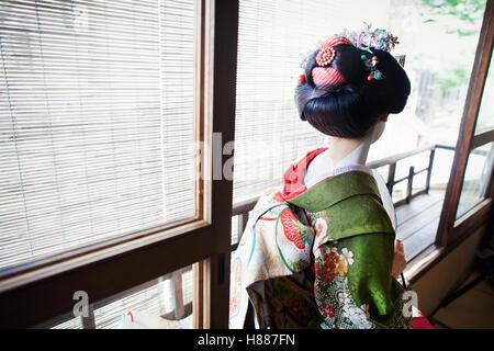 Eine Frau gekleidet im Geisha-Stil in einem Kimono und Obi mit einem aufwendigen Frisur und blumige Haarspangen mit weißem Gesicht Make-up. Stockfoto