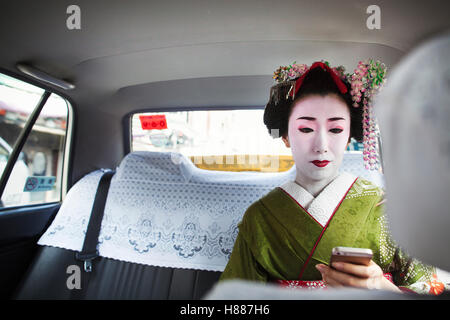 Eine Frau gekleidet in traditionellen Geisha-Stil in einem Taxi mit einem Smartphone. Stockfoto