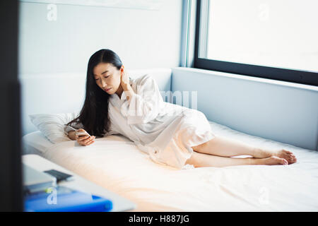 Eine Frau im Bett in einem Hotel mit ihrem Smartphone. Stockfoto