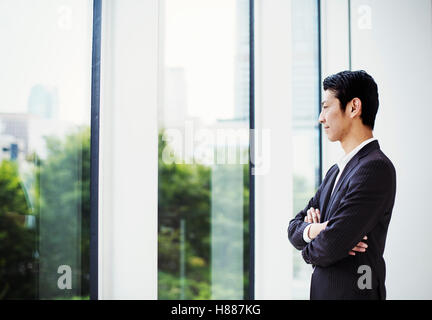 Ein Geschäftsmann im Büro durch ein großes Fenster mit Blick. Stockfoto