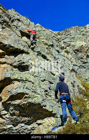 Mann Sicherungstechnik Kind auf einer Felswand klettern am Sewenhütte, Kanton Uri, Schweiz Stockfoto