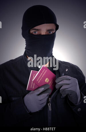 Mann trägt eine Sturmhaube und hält Fremde Pässe, symbolisches Bild für illegale Einwanderer Stockfoto