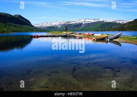 Eine Landschaft in Norwegen mit mehreren bunten Booten trocknen am Ufer eines Sees, umgeben von Bergen. Stockfoto