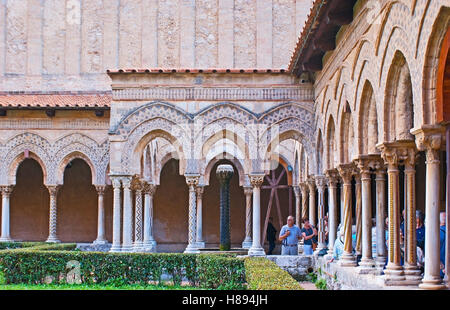 Die schwarze Zick-Zack-geschnitzte Spalte auf den alten arabischen Brunnen im Kreuzgang von Monreale-Garten, umgeben von Steinbögen, Sizilien Stockfoto