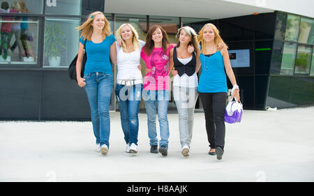 Fünf Mädchen im Teenageralter gehen Arm in Arm, vor einem Gebäude Stockfoto