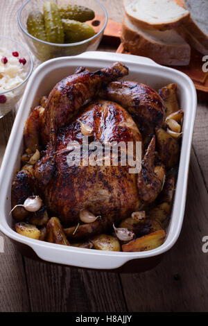 Hausgemachte ganzes Brathähnchen serviert mit Gurken und Sauerkraut auf rustikalen Holztisch für Abendessen, erhöhte Ansicht Stockfoto