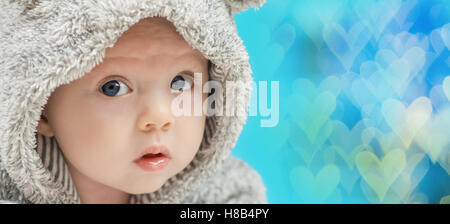 Nahaufnahme des schönen glückliches Baby mit blauen Augen in grau tragen wie ein Kleidungsstück auf blau herzförmige Hintergrund Stockfoto