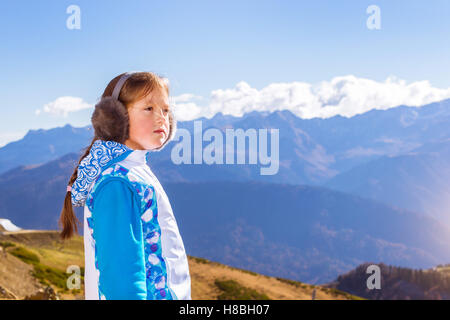 Mädchen mit einem Zopf, gekleidet in Sportjacke und warmen flauschigen Kopfhörer bewundert herbstliche Berglandschaft, Sotschi, Russland Stockfoto