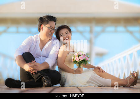Porträt von fröhlichen Brautpaar umarmt und in die Kamera schaut. Asiatische Hochzeitspaar in Brücke in der Nähe von Meer. Stockfoto