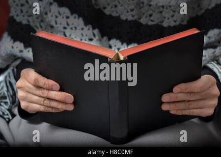 Hände von Frau mittleren Alters kaukasischen tragen Winterkleidung und eine Decke hält ein schwarzes Buch Stockfoto