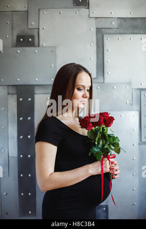 Schöne junge schwangere Frau im schwarzen Kleid mit roten Rosen Stockfoto