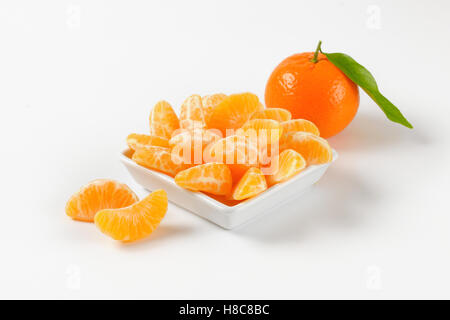 Schüssel mit Mandarine Segmente und ganze Mandarine auf weißem Hintergrund Stockfoto