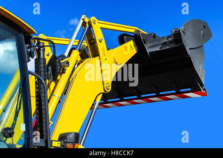 Leuchtend gelbe Traktor-Loader auf einem Hintergrund von den klaren blauen Himmel, Kabine mit der angehobenen Pfanne hautnah Stockfoto