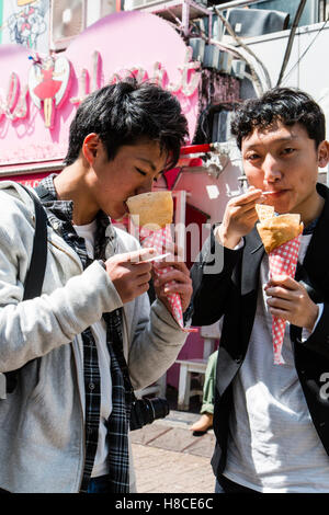 Japan, Tokio, Harajuku, Takeshita-dori. Zwei Teenager japanische Männer halten und essen Crepes in Kegel, auf Viewer. Angel's Herz Crêpe-Store. Stockfoto