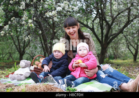 Mutter mit Zwillingen auf Plaid im Freien im Apfelgarten Stockfoto