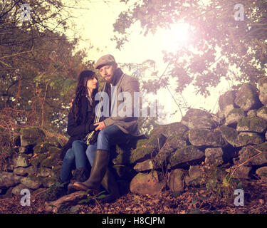 Young 30 Paar sitzt auf Stein Wand im Herbst Einstellung Stockfoto