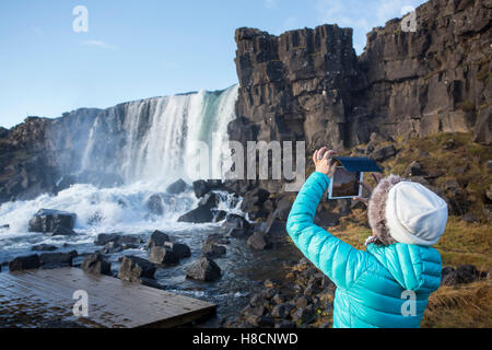 Touristen fotografieren und beobachten Sie den Wasserfall in Pingvellir Nationalpark bekannt als Oxarafoss vom Fluss Oxara. Stockfoto