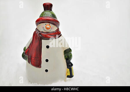 Keramik Figur einen Schneemann mit rotem Schal oder Schalldämpfer und Laterne auf Schnee Hintergrund, Nahaufnahme, Platz für text Stockfoto