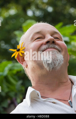 Lächelnder älterer Mann mit Blume hinter dem Ohr Stockfoto