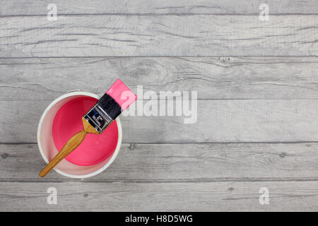 Geladenen Pinsel über eine weiße Farbe Wasserkocher gelegt gefüllt mit rosa Farbe auf grau shabby Stil Holzfussboden Stockfoto