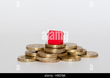 Eine kleine Plastikmodell rote Haus oben auf einem Stapel von Pfund-Münzen.  Gehäusekonzept Finanzen. Stockfoto