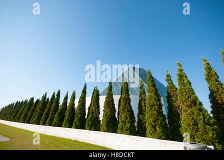 Eine Reihe Zedern auf dem weitläufigen Gelände von Torontos Aga Khan Park und Museum mit dem Ismaili Centre und Jamatkhana im Hintergrund. Stockfoto