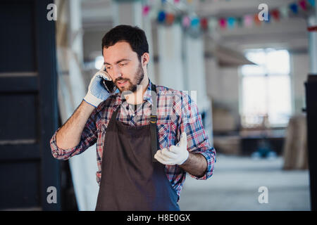 Austausch von Ideen. Glücklich Jüngling telefonieren mit dem Handy stehen in seiner Werkstatt Stockfoto