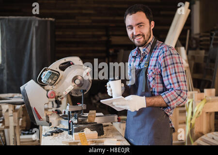 Zimmermann, eine Kaffee-Pause halten Notebook vor Kreissäge in seiner Werkstatt Stockfoto