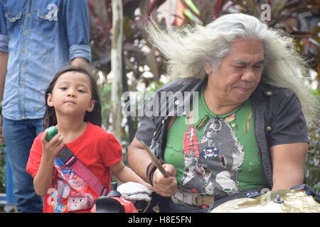 Malaysische Mann mit weißen langen Haaren spielen Musik auf der Straße mit seiner Nichte in Kuala Lumpur, Malaysia Stockfoto