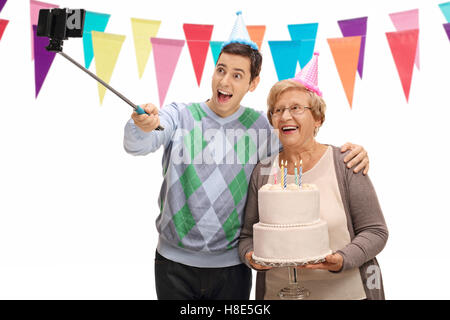 Junger Mann und eine reife Frau mit Partyhüte und einen Geburtstagskuchen, wobei ein Selbstporträt mit einem Stock isoliert auf weißem Hintergrund Stockfoto