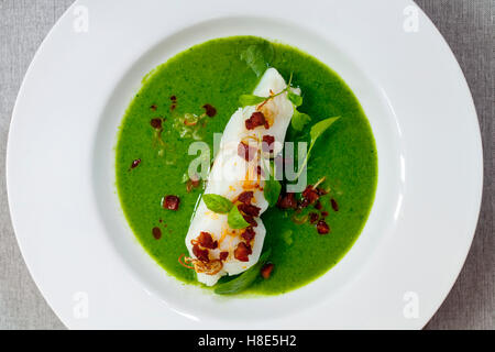 Butter Pochierter Kabeljau mit grünen Erbsen, Spinat und Basilikum Veloute, knusprige Chorizo und Schalotten Stockfoto