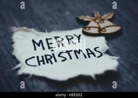 Nahaufnahme von einem Blatt Papier mit dem Text Frohe Weihnachten handschriftlich in es und ein Holz Ornament auf einem rustikalen Holzoberfläche Stockfoto