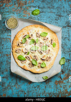 Hausgemachte Pilz-Pizza mit Basilikum Blätter und Gewürze im Glas auf Backpapier über blau rustikal aus Holz dunkel, Ansicht von oben, Stockfoto