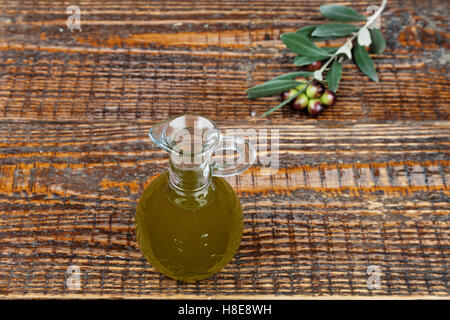 Olivenöl in Glasflasche und Zweig der Oliven auf den Tisch Stockfoto